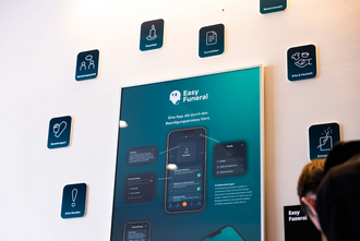 Ausstellungsplakat zur App „Easy Funeral“, umgeben von Icons zu Schritten einer Bestattung.
