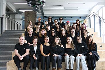 Das studentische Team des DPWK 2026: Rund 25 Studierende sitzen auf eine Holztreppe © DPWK/Kaja Schiller