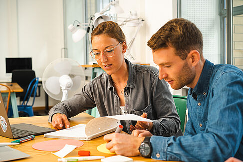 Zwei Studierende arbeiten konzentriert mit Laptop, Collegeblock, Stiften und Notizzetteln