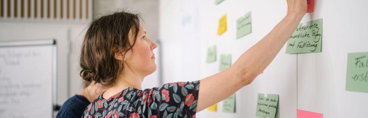 Junge Frau klebt bunte Post-Its an eine Wand