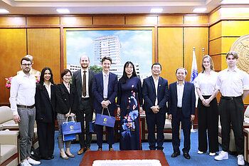 Dressed in formal attire, some members of the tour group pose for a group photo in a room with representatives from the Hanoi Law University