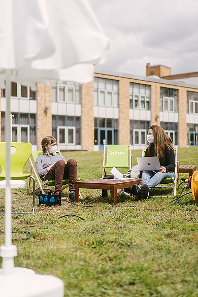 Zwei Studierende mit Mund-Nasen-Schutz sitzen mit Carpe-Campus-Equipment auf dem Campus Wilhelminenhof