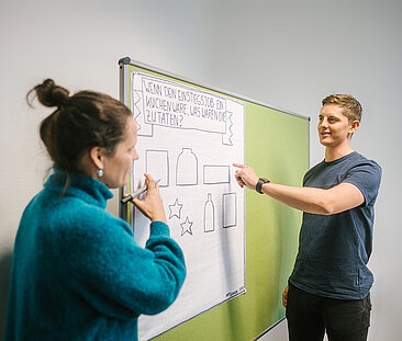 Two people confer at a pinboard