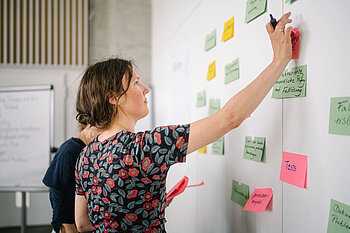Junge Frau klebt beschriftete bunte Post-Its an eine Wand