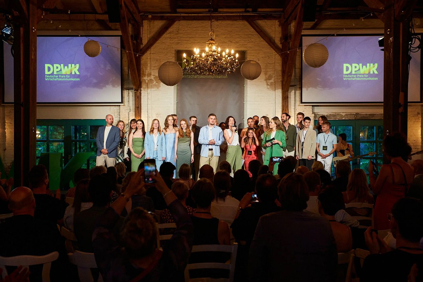 Ein Gruppe Menschen auf einer Bühne in einem festlichen Raum, im Hintergrund zwei Bildschirme mit dem Schriftzug "DPWK 2025" © DPWK