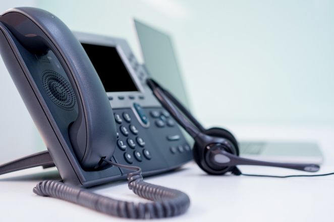 Schwarzes Büro-Telefon, daneben ein Headset und ein Laptop © istockphoto.com/Chainarong Prasertthai