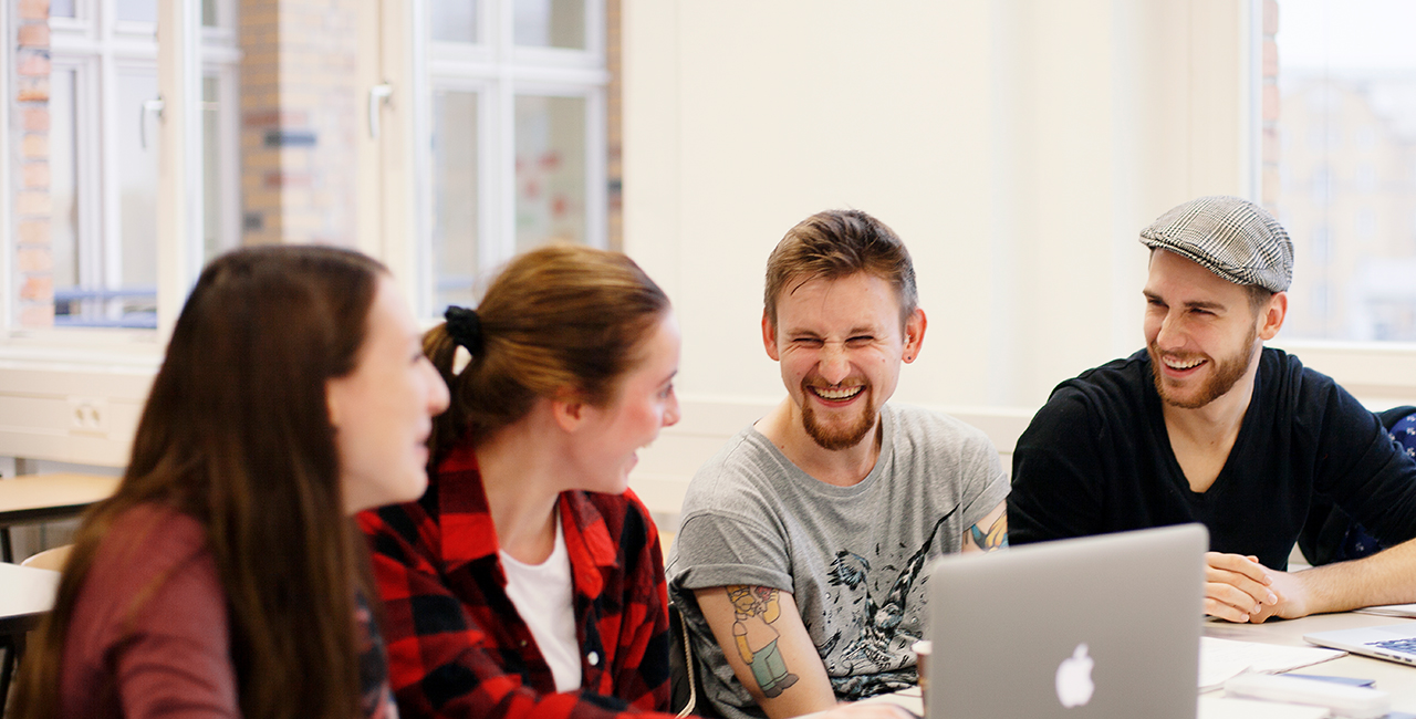 Studierende im Gespräch, vor ihnen ein Laptop