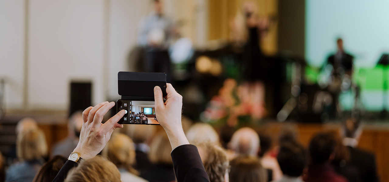 Veranstaltung im Audimax, jemand aus dem Publikum fotografiert die Bühne mit einem Smartphone