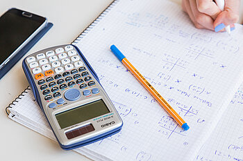 Taschenrechner, Tisch und Arbeitsblatt mit Mathe-Aufgaben