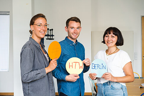 Drei Studierende, die runde Schilder mit der Aufschrift "#HTW Berlin" hochhalten