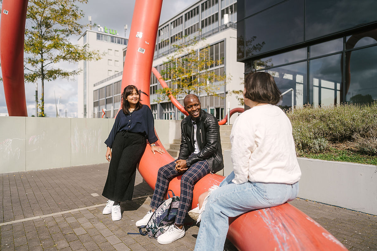 Drei Studierende sitzen auf dem Kunst am Bau auf dem Campus Wilhelminenhof