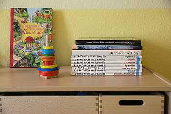 Auf einem Regal im Familienzimmer stehen Spielzeug, Bücher und weitere Materialien für Kinder.