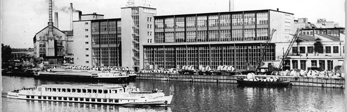 Blick vom anderen Spreeufer auf das Wasser mit einem Ausflugsdampfer und die Produktionshallen des Kabelwerkes Oberspree.