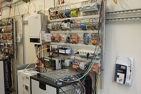 Bunte Kabel, verschiedene Geräte und Stecker sind beim Prüfstand für das Energiemanagement zu sehen.