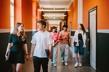 Eine Gruppe Studierender läuft gemeinsam durch einen rot gestalteten Hochschulflur.