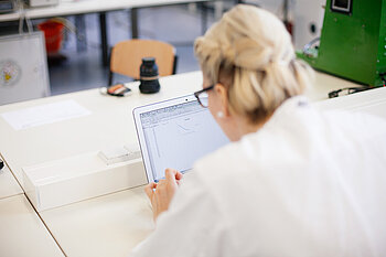 Forscherin im Laborkittel am Laptop