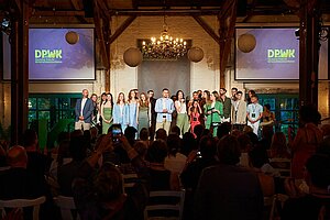 Bühne mit festlicher Beleuchtung, darauf viele Menschen © DPWK