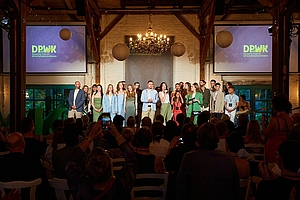 Ein Gruppe Menschen auf einer Bühne in einem festlichen Raum, im Hintergrund zwei Bildschirme mit dem Schriftzug "DPWK 2025" © DPWK