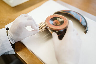 Hände mit weißen Stoffhandschuhen arbeiten mit Scherben