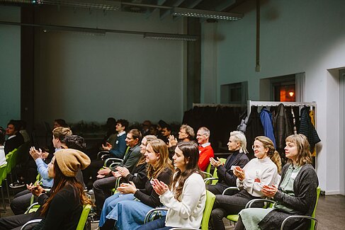 Klatschende Personen in mehreren Stuhlreihen, den Blick nach vorne gerichtet