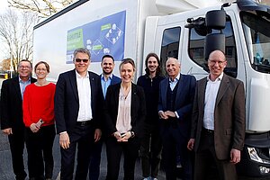 Acht Personen stehen nebeneinander vor einem Transporter 