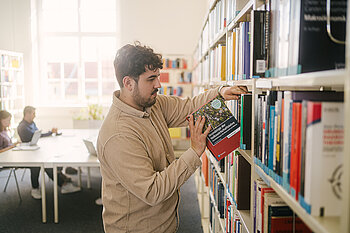 Student holt aus einem Bücherregal in der Bibliothek ein Buch