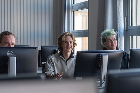 Drei lachende junge Menschen hinter Monitoren © O ja! Orientierungsjah