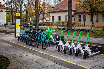 Foto eines Jelbi-Punkts in Berlin: Jelbi Schild, daneben Leihfahrräder und Scooter auf einer markierten Abstellfläche © BVG Foto eines Jelbi-Punkts in Berlin: Jelbi Schild, daneben Leihfahrräder und Scooter auf einer markierten Abstellfläche © BVG