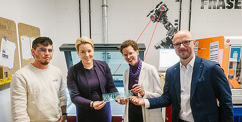 Franziska Giffey, Stefanie Molthagen-Schnöring und Sebastian Stietzel halten ein gerade erstelltes Plexiglas-Schild "KMU-Büro" in den Händen. Links daneben die SHK Tomas Salimbeni.