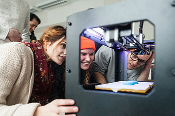 Drei Studierende schauen auf einen 3D-Drucker