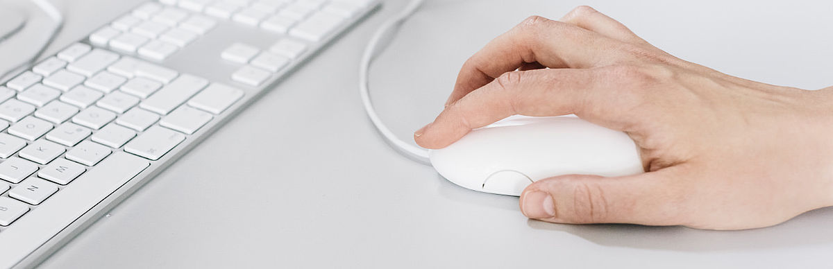 Hand auf einer Computermaus mit Tastatur