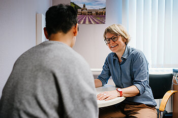 Eine Mitarbeiterin sitzt einem Studenten an einem Tisch gegenüber und spricht mit ihm.