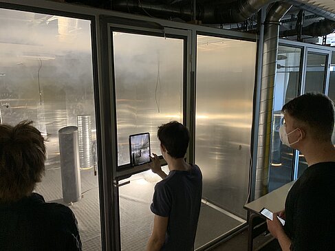 3 Studierende stehen vor einer Glaswand und beobachten Rauch in einem Labor © HTW Berlin/O ja!