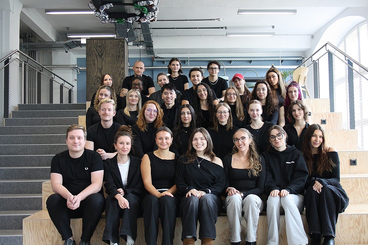 Das studentische Team des DPWK 2026: Rund 25 Studierende sitzen auf eine Holztreppe © DPWK/Kaja Schiller