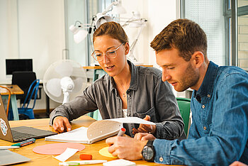 Zwei Studierende arbeiten konzentriert mit Laptop, Collegeblock, Stiften und Notizzetteln 