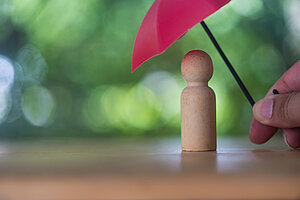 Eine Hand hält einen Schirm über eine Holzspielfigur © istockphoto.com/dontree_m