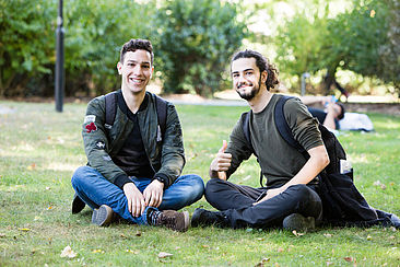 Zwei internationale Studenten sitzen auf der Wiese auf dem Campus Treskowallee