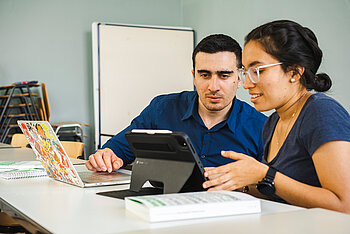 Zwei Studierende, die gemeinsam auf ein Tablet schauen