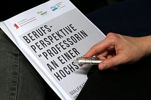 Eine Person hält ein Programmheft mit dem Titel "Professorin an einer HAW" © HWR Berlin/Sylke Schumann