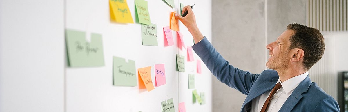 Männlicher Professor klebt Sticky Note auf eine weiße Tafel