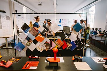 Broschüren, Plakate und Designobjekte bei der Werkschau - im Hintergrund verschwommen Personen © HTW Berlin/Alexander Rentsch