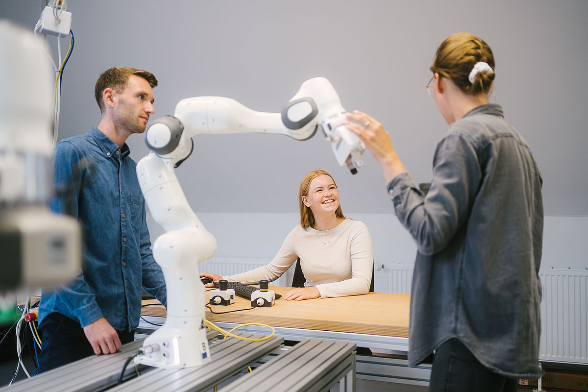 Drei Studierende arbeiten mit einem Roboter
